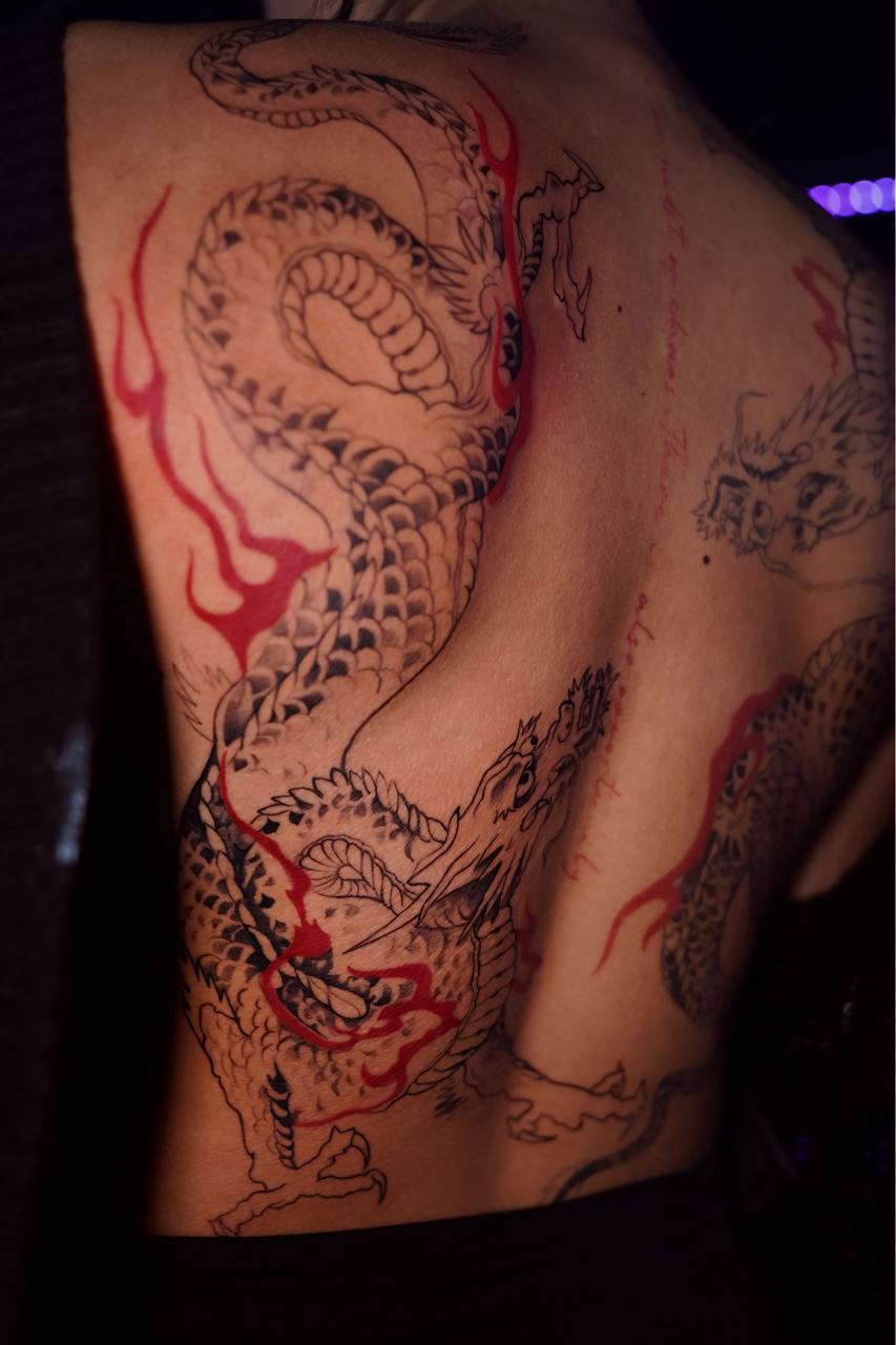 Fine line dragon tattoo with red accents